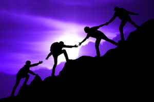 Image of 4 people with arms reaching towards each other in a chain to help each other climb a mountain