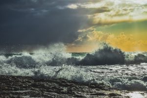 A stormy scene at sea, but the sun is beginning to break in the distance suggesting hope.