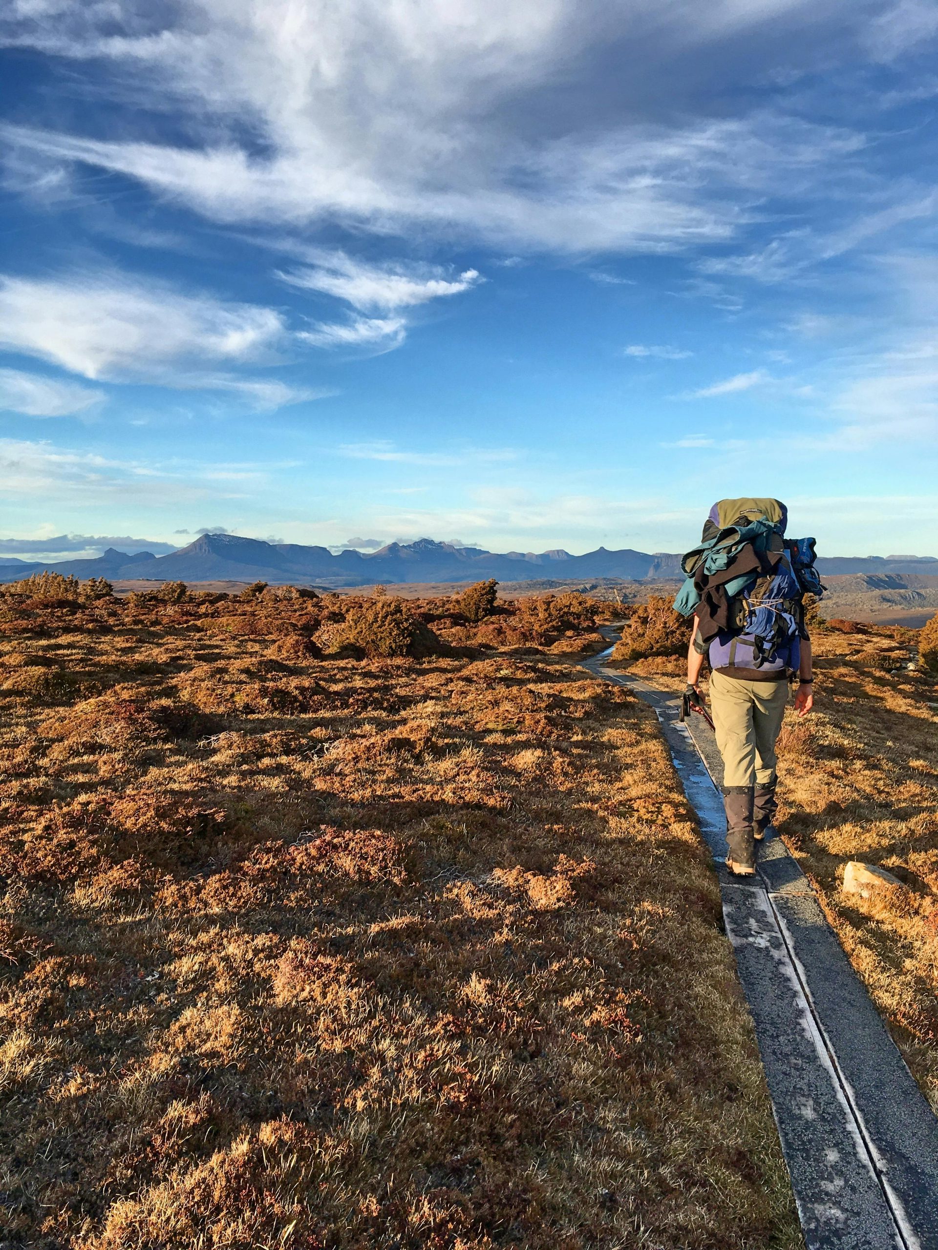 A person walking along a track carries a heavy rucksack