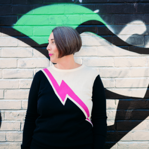 Photo of Helen Burness in a striking black, white and pink top against a black, white and green wall